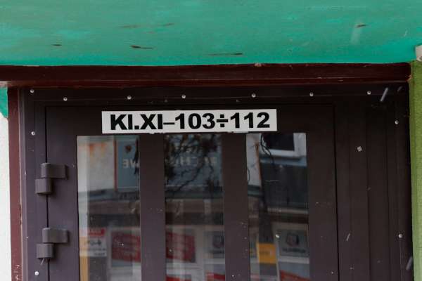 Cedulka nad vchodovými dveřmi do bytovky s nápisem KI.XI–103÷112