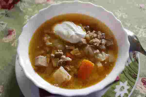 Čirá (ale hustá) polévka s kostkami masa, kusy mrkve, bílého zelí, s kroupami a ostrůvkem smetany.